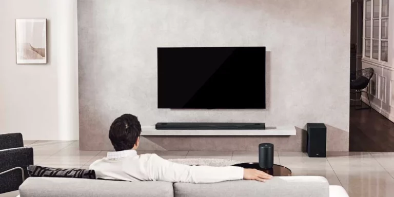 Hombre sentado en sofá frente a televisor con barra de sonido LG y subwoofer en el salón